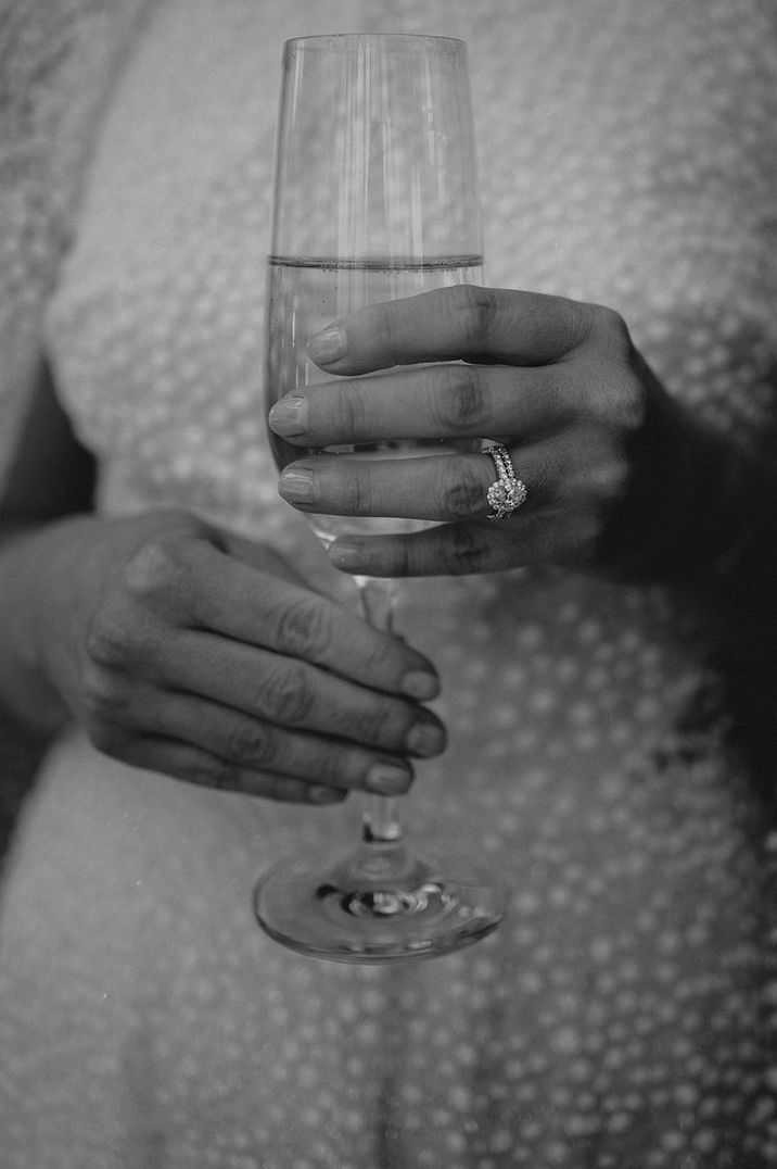 Bride in lace wedding dress holding champagne glass with oval pave halo engagement ring 