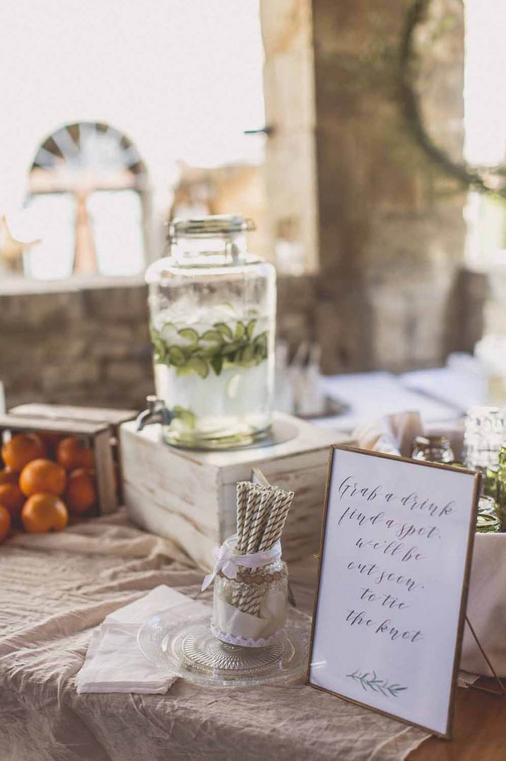 Wedding drink hydration station with glass dispenser full of drinks and lime with striped paper straws and signage 