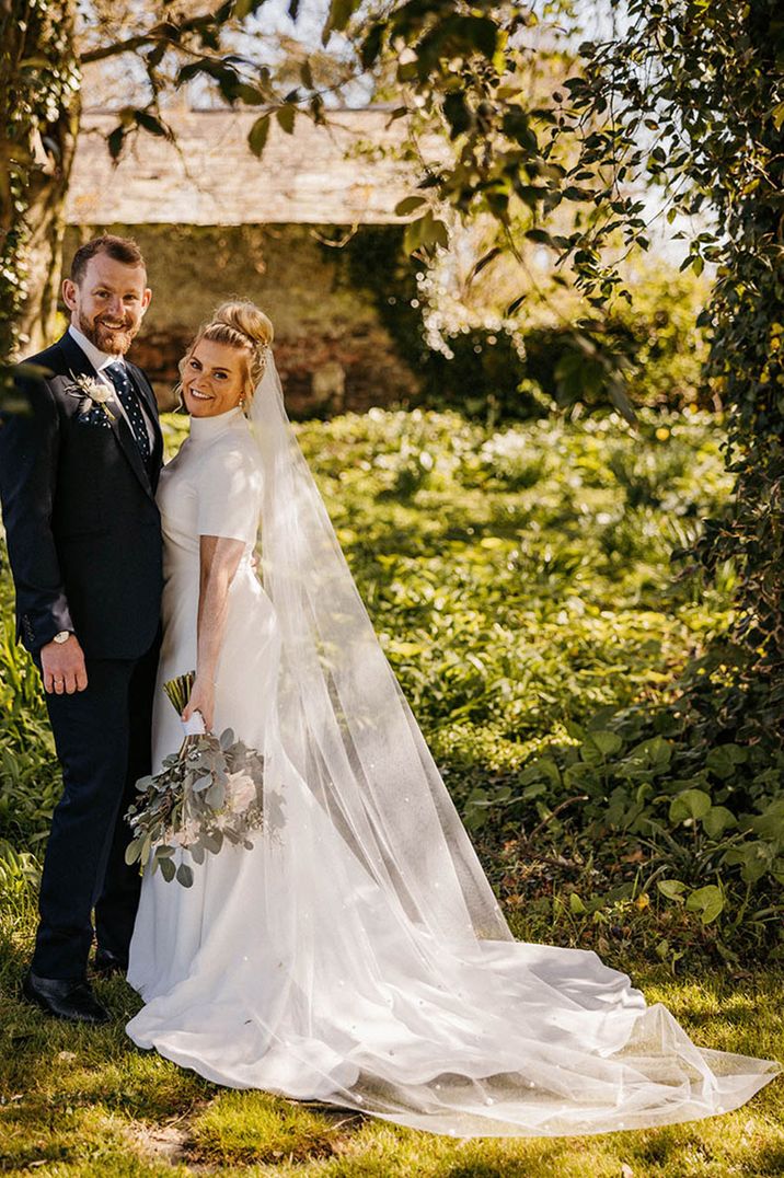 Groom in navy blue suit with the bride in a short sleeve high neck wedding dress 