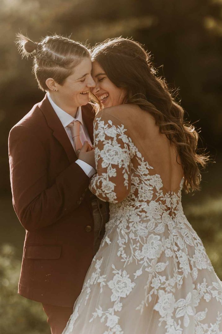 Bride in pretty open back illusion sleeve wedding dress at golden hour embracing bride in burgundy suit 