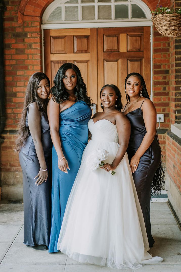 Black bride in a strapless princess wedding dress standing with her bridesmaids in different navy and blue satin bridesmaid dresses 