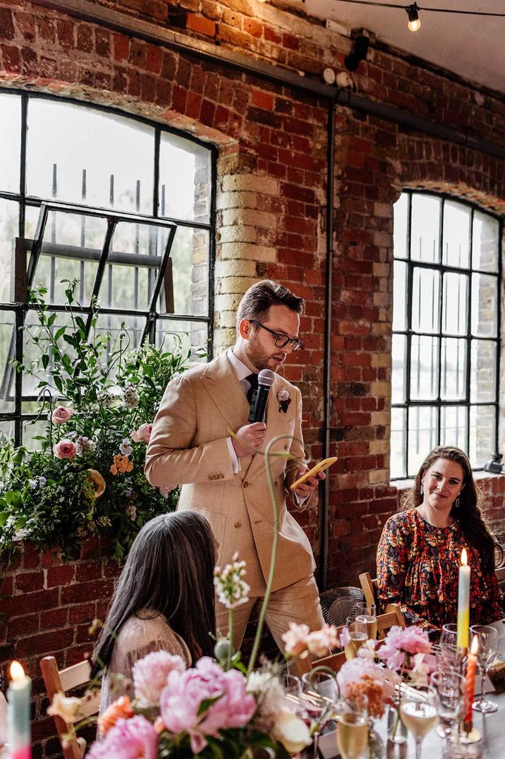 Man in cream suit and black tie giving speech at Loft Studios wedding