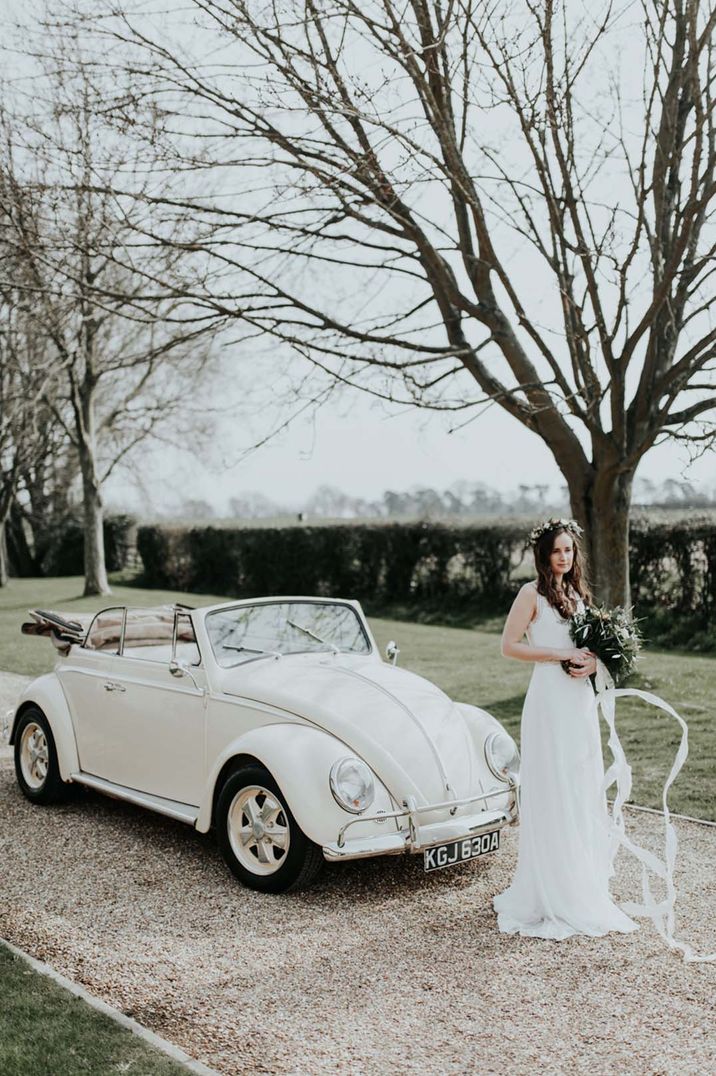 Bride in flower crown and sleeveless wedding dress standing by cream VW Beetle