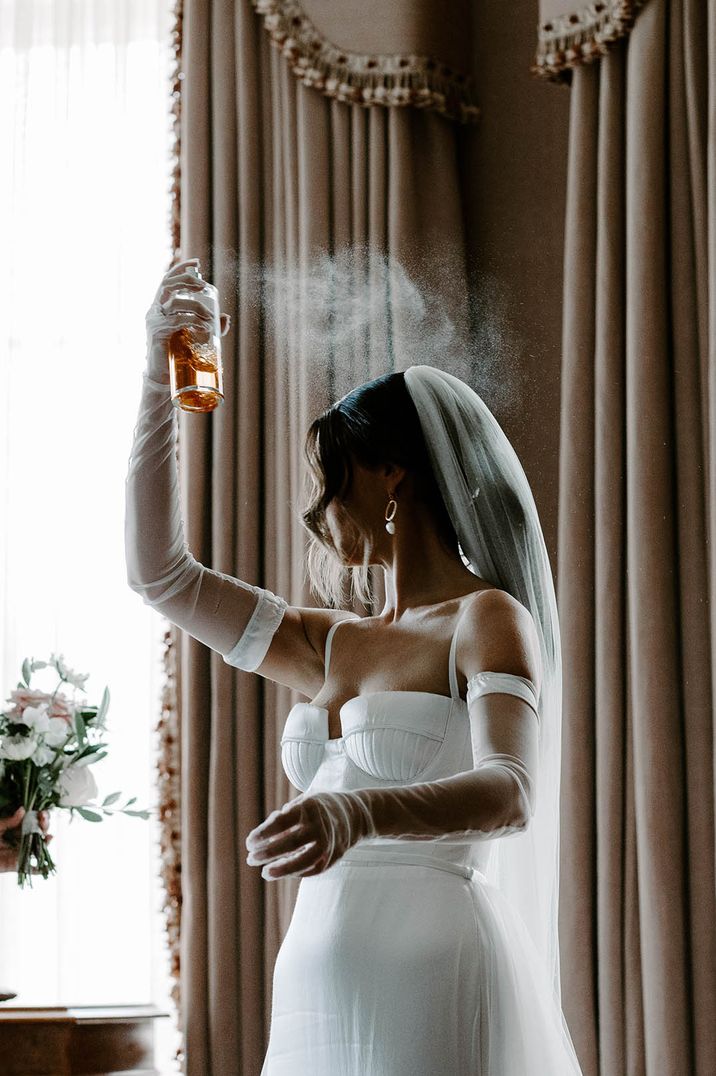 Bride on wedding morning spraying perfume with sheer gloves on 