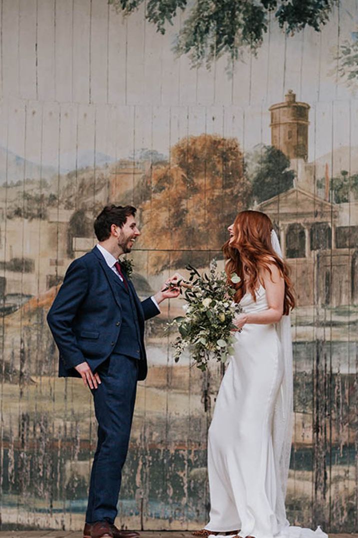 Bride in white satin cowl neck wedding dress laughing with the groom in navy suit 