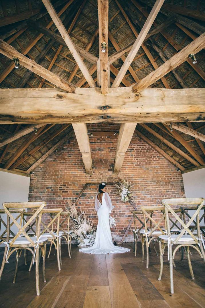 Bride in puddle train wedding dress standing in The Brickhouse Vineyard reception room with exposed beams 