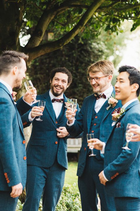 The groom and groomsmen enjoy a drink together before the wedding in matching blue suits 