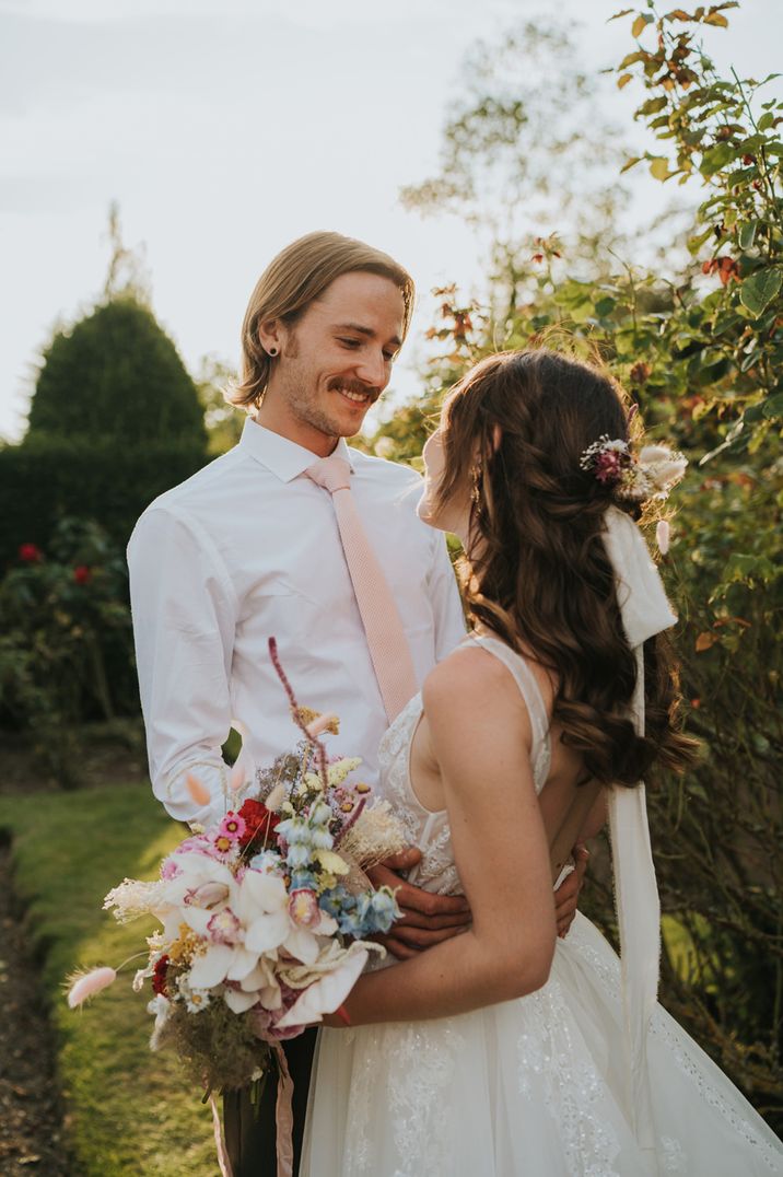 Bride and groom portrait with bride in a Monique lhuillier wedding dress with half up half down hair holding a mixed flower bouquet 