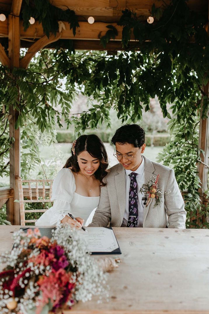 Asian bride and groom signing the resister at their intimate outdoor wedding at The Secret Garden wedding venue 