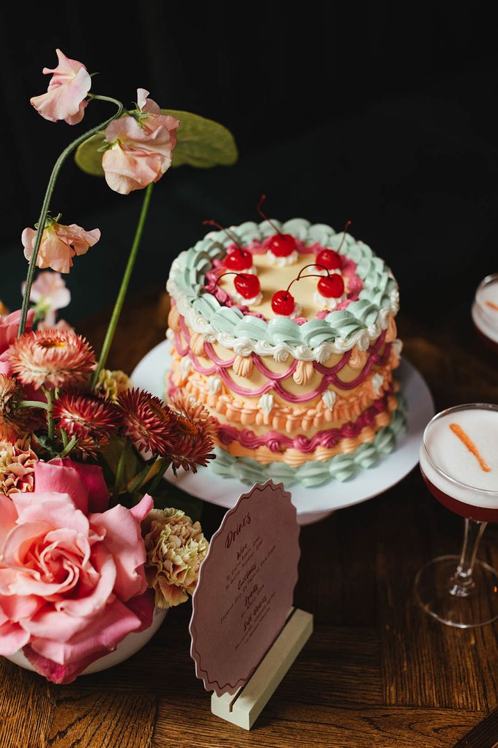 Single tier retro wedding cake with mint green, lemon, pink, white and orange icing topped with cherries 