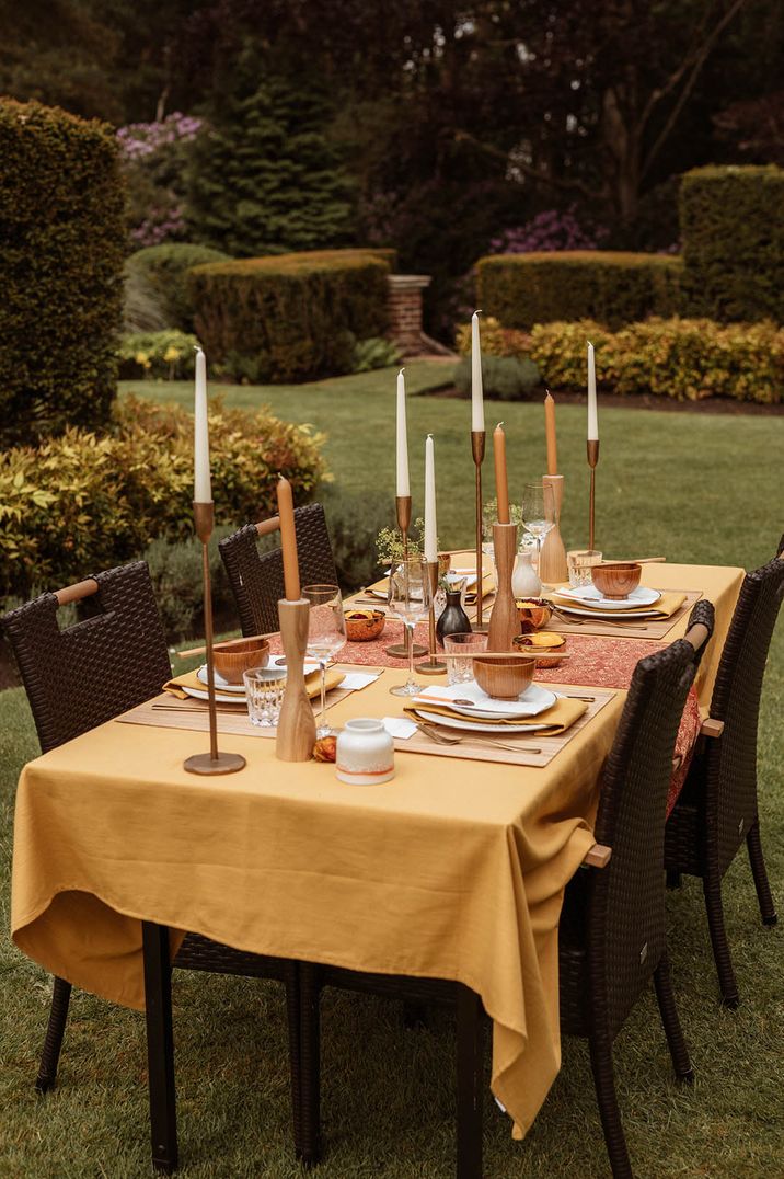 Brown woven chairs with yellow tablecloth table setting with white and brown candles and rice bowls by The Props Library