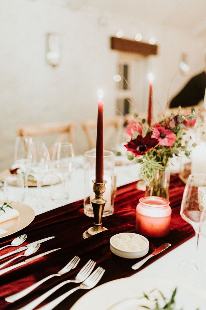 Red velvet table runner with red taper candles and gold hardware for a Christmas winter wedding tablescape 