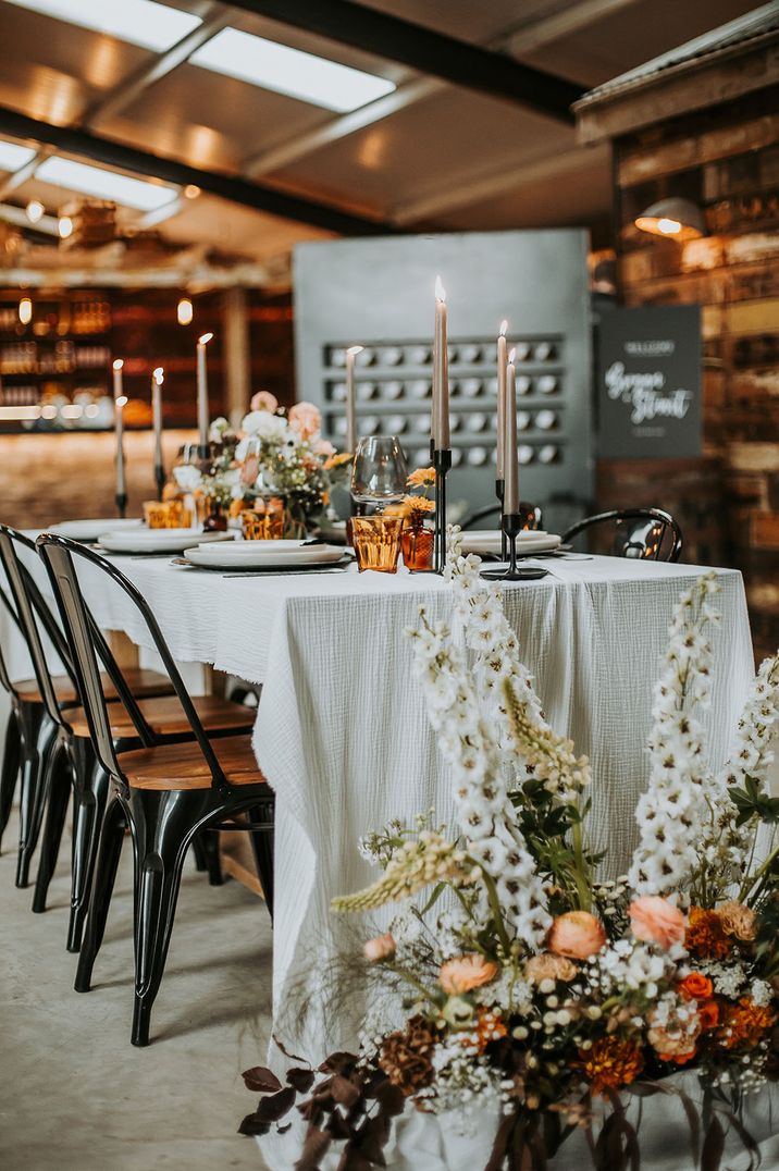 Moody wedding tablescape with coloured glassware with neutral flowers and a white tablecloth 