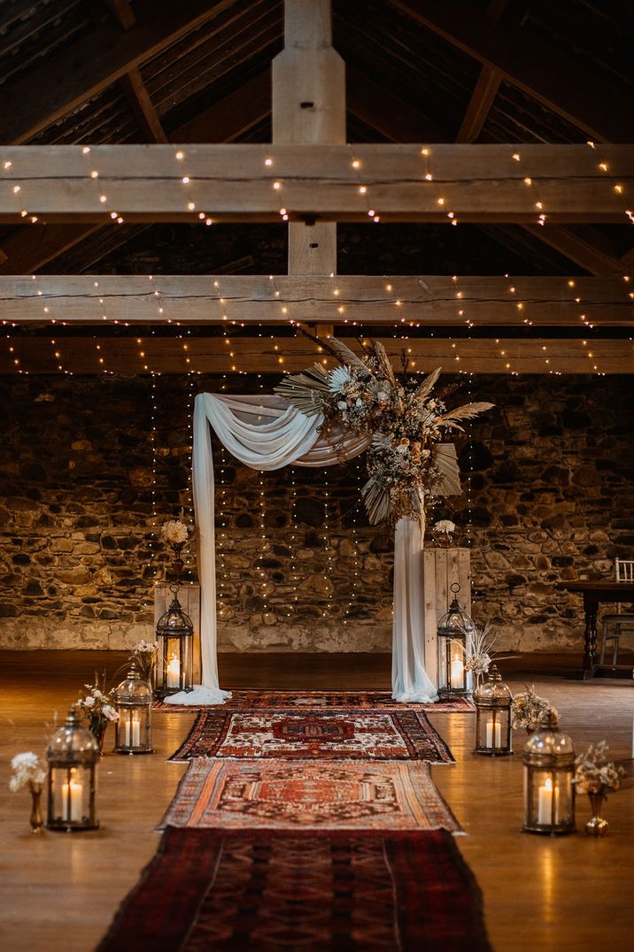 Wedding ceremony room at rustic wedding venue with white drapery in statement altar decoration lined with lanterns 