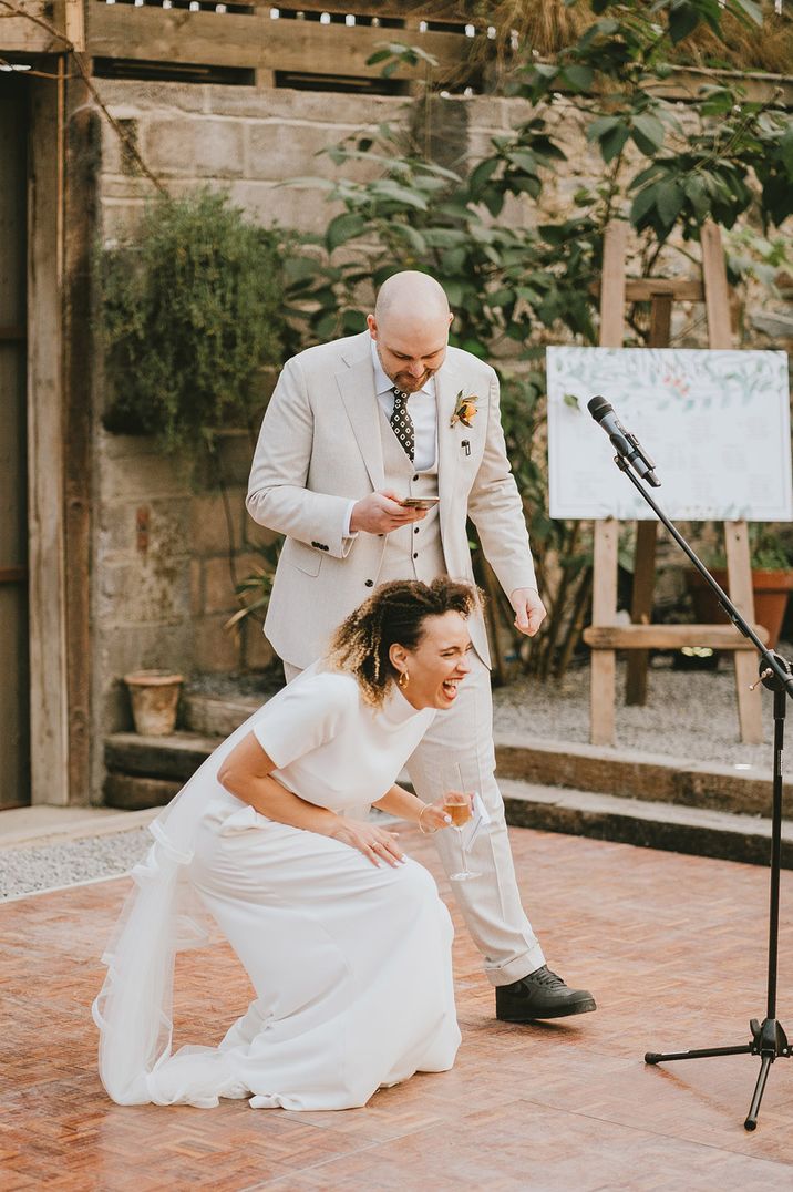 Bride in two piece outfit is laughing during the joint speech with groom in light toned suit 