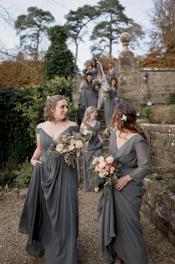 Bridesmaids in different grey dresses holding peach rose bouquets 