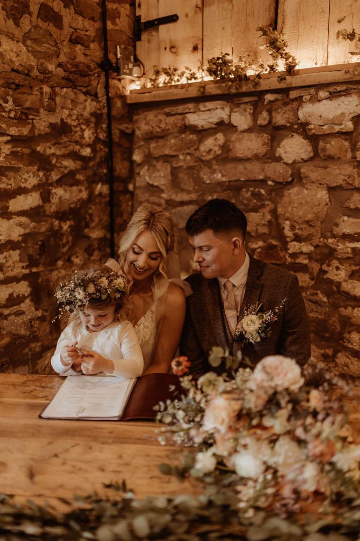 Bride, groom and their daughter signing the register at their intimate Eden Barn wedding 