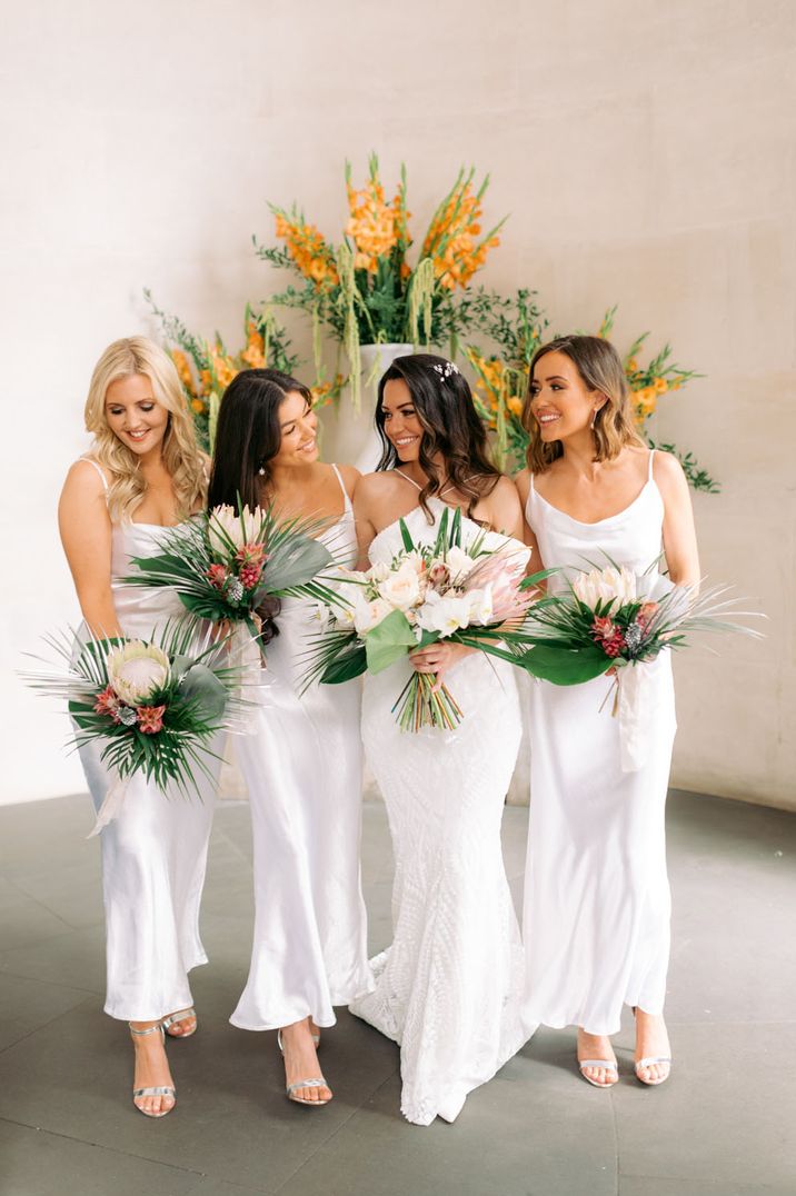 Bridal party with large exotic flower bouquets and long satin white bridesmaid dresses