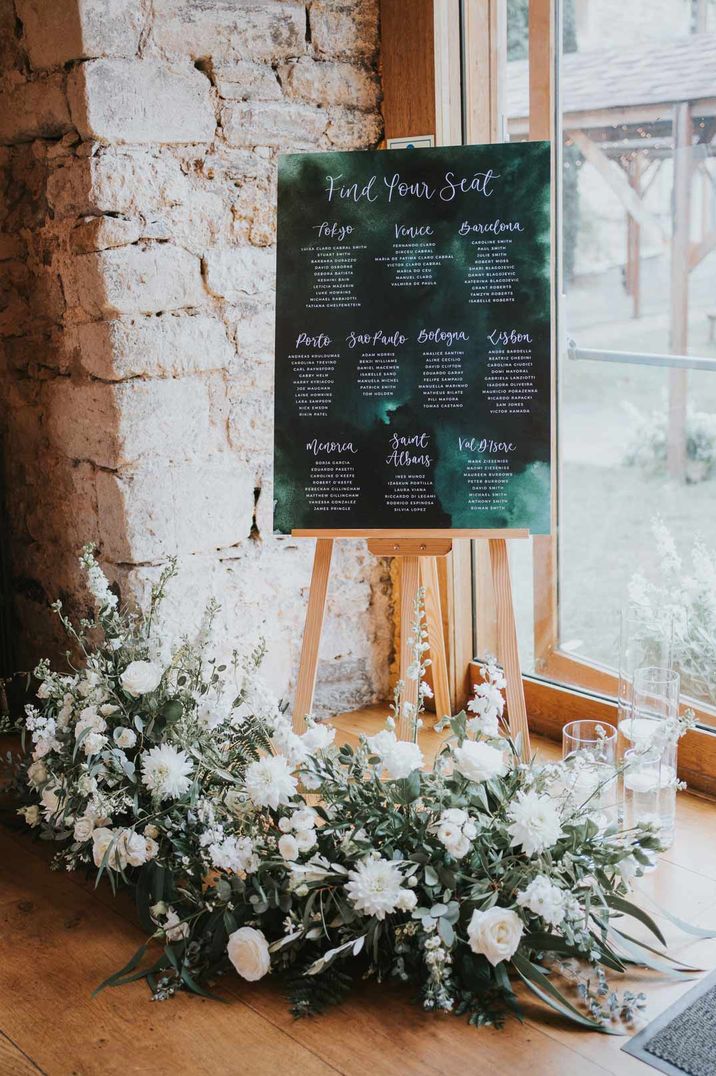 Wedding table plan on wooden easel with white rose foliage decorations at mixed gender wedding party