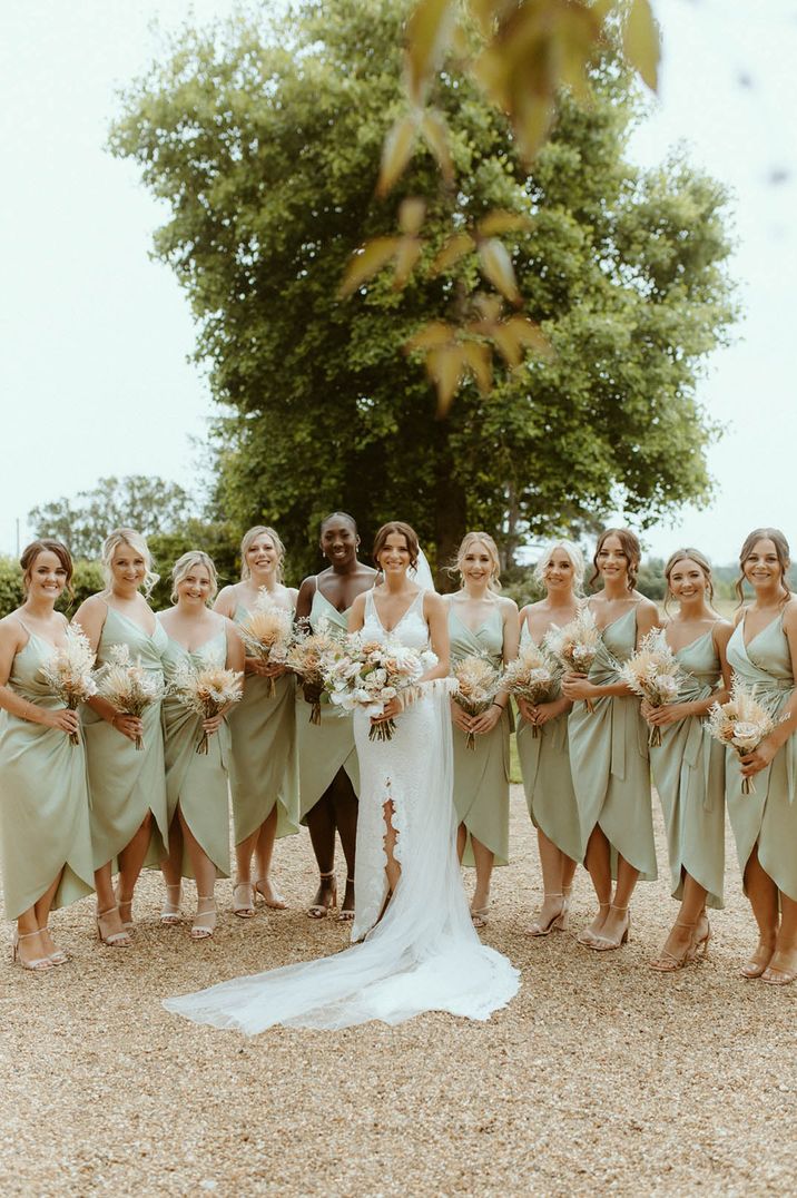 Bridal party with the bridesmaids wearing sage green satin wrap bridesmaid dresses with the bride in a fitted lace wedding dress holding boho bouquets for wedding under 40k