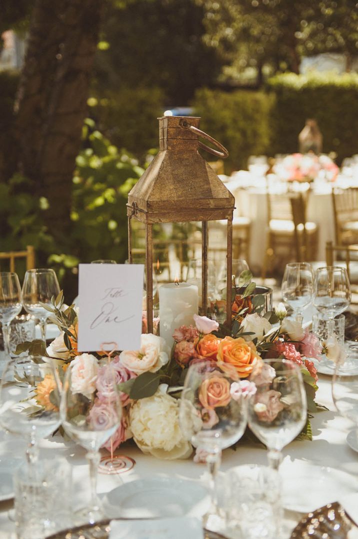 Rustic candle lantern wedding table centrepiece with white pillar candle surrounded by orange and pink flowers