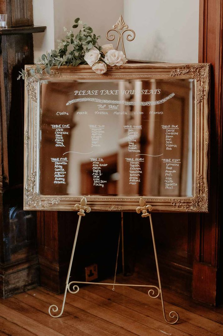 Mirrored wedding table plan in large gold frame at Holmewood Hall with white rose and eucalyptus decorations on top 