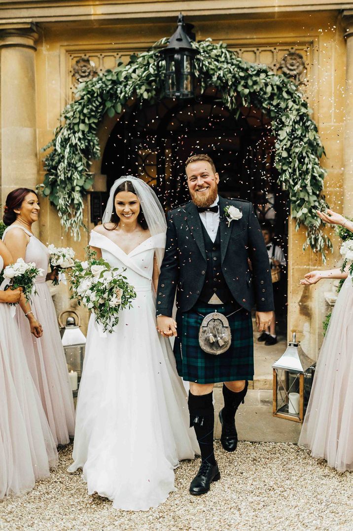 Bride in princess wedding dress and groom in a tartan kilt surrounded by wedding party