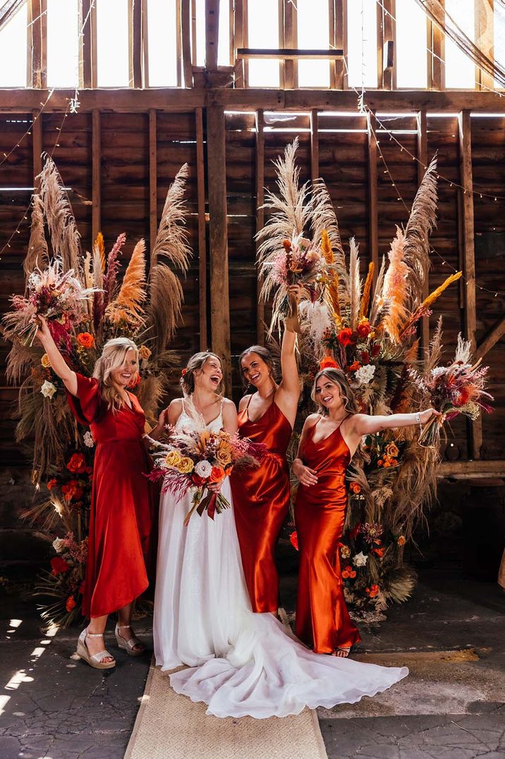 Bride with bridesmaids in burnt orange satin dresses with dried flower decor