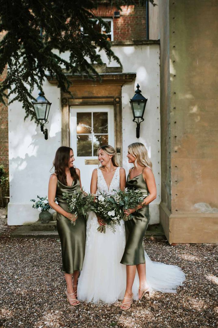 Bride in deep v neck princess wedding dress standing with bridesmaids in cowl neck sage green midi bridesmaid dresses 