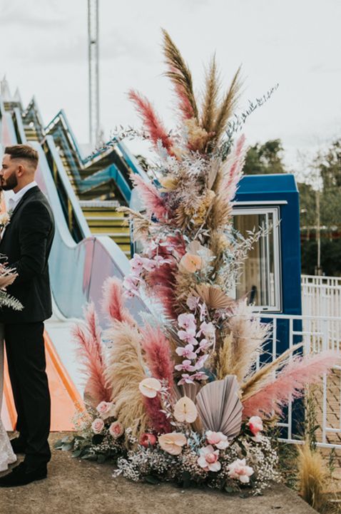 Colourful pink pampas grass columns wedding decor with bride and groom posing in front of colourful slides 