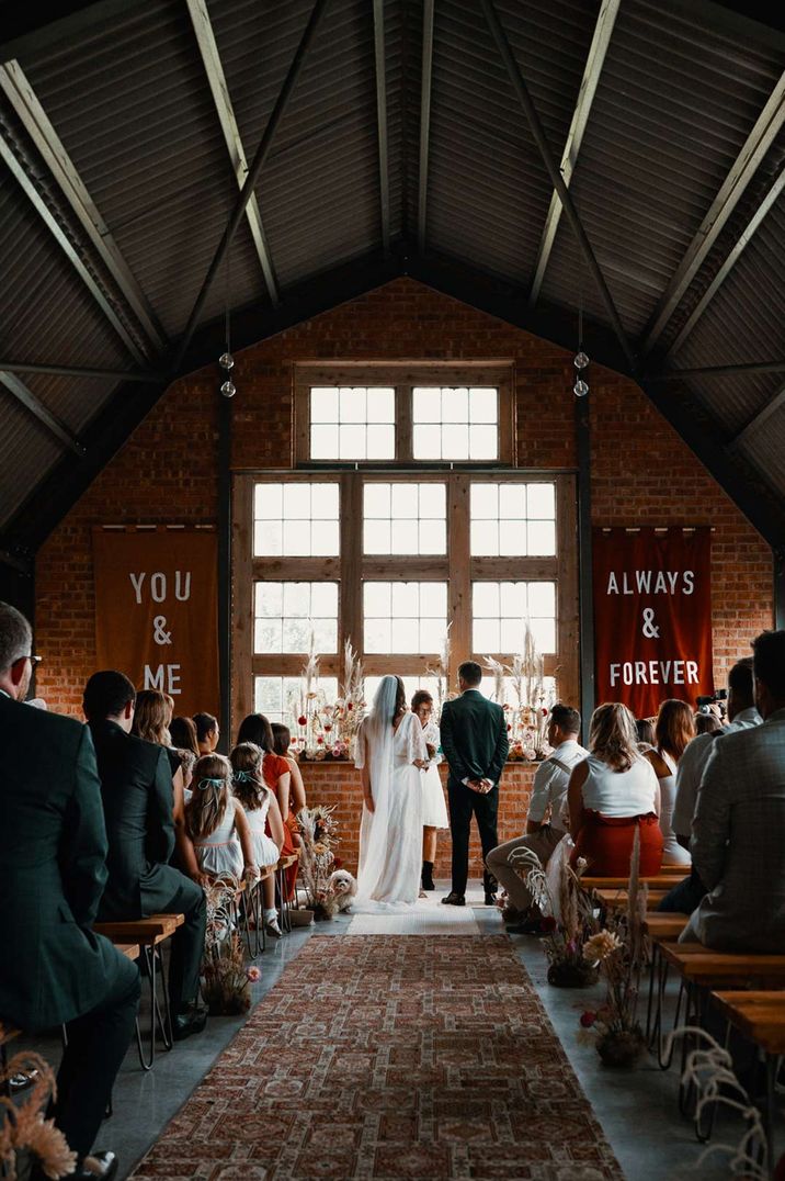 Bride and groom standing at the alter underneath the square window display at The Giraffe Shed quirky wedding venue