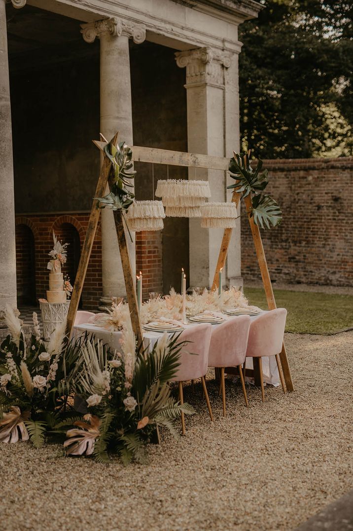 Tropical wedding flower arrangements with dried wedding flowers, and palm leaves at outdoor wedding table setting with pink chairs 