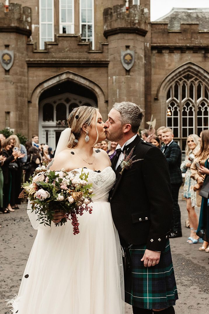 Scottish wedding with the bride and groom sharing a kiss as they are covered in black confetti 