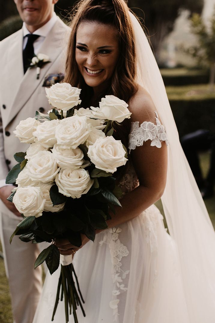 Bride in off the shoulder wedding dress with white rose wedding bouquet inspired by June birth flowers 