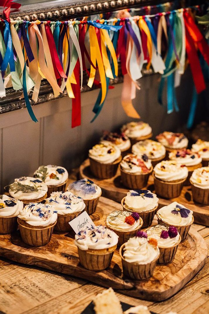 Tray of flavoured cupcakes with white frosting decorated with edible flowers 