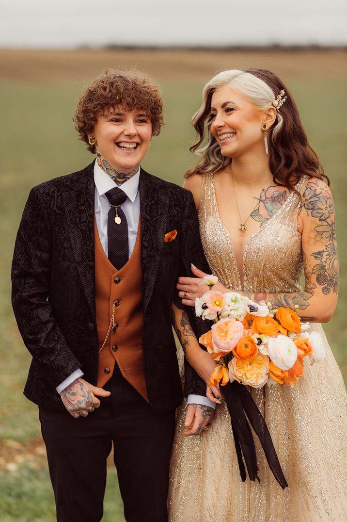 LGBQTIA+ wedding inspiration with bride wearing a gold wedding dress with orange and yellow wedding bouquet and bride in snake skin suit jacket 