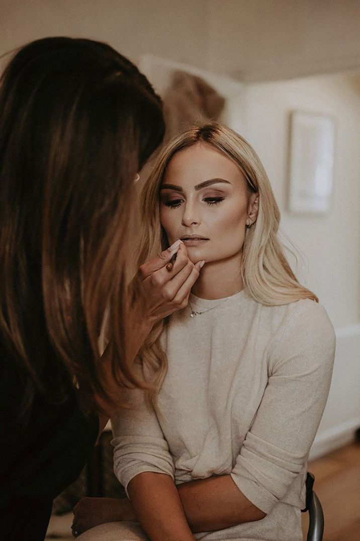 Bride sits to get her makeup done for the wedding day 