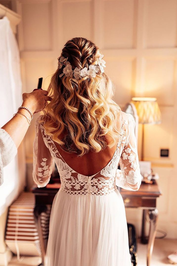 Bride wearing her blonde curled hair in half up half down wedding hairstyle with white flower hair accessory