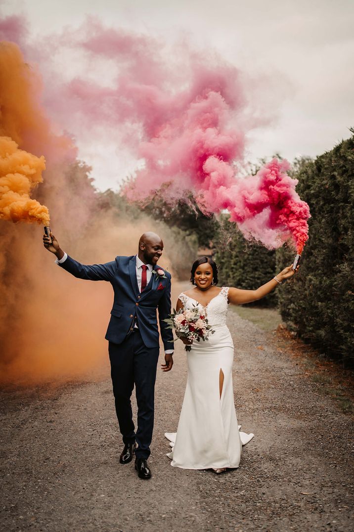 Black bride and groom holding orange and pink smoke flares 