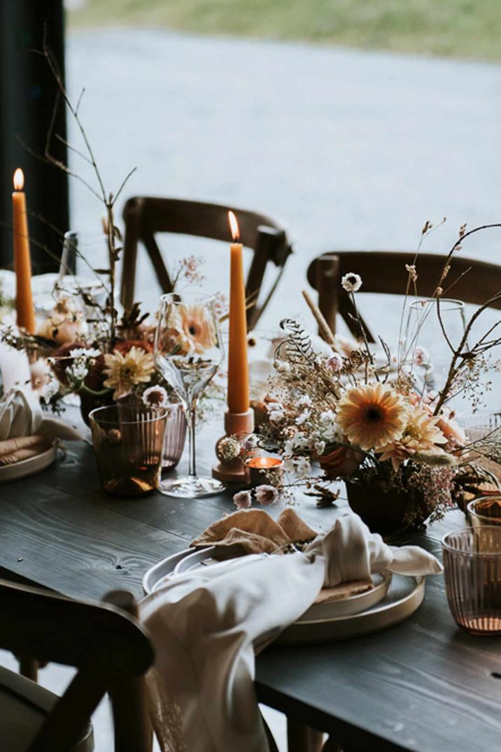 Autumnal and colourful wedding tablescape with orange candles and colourful floral arrangements with decorative twigs