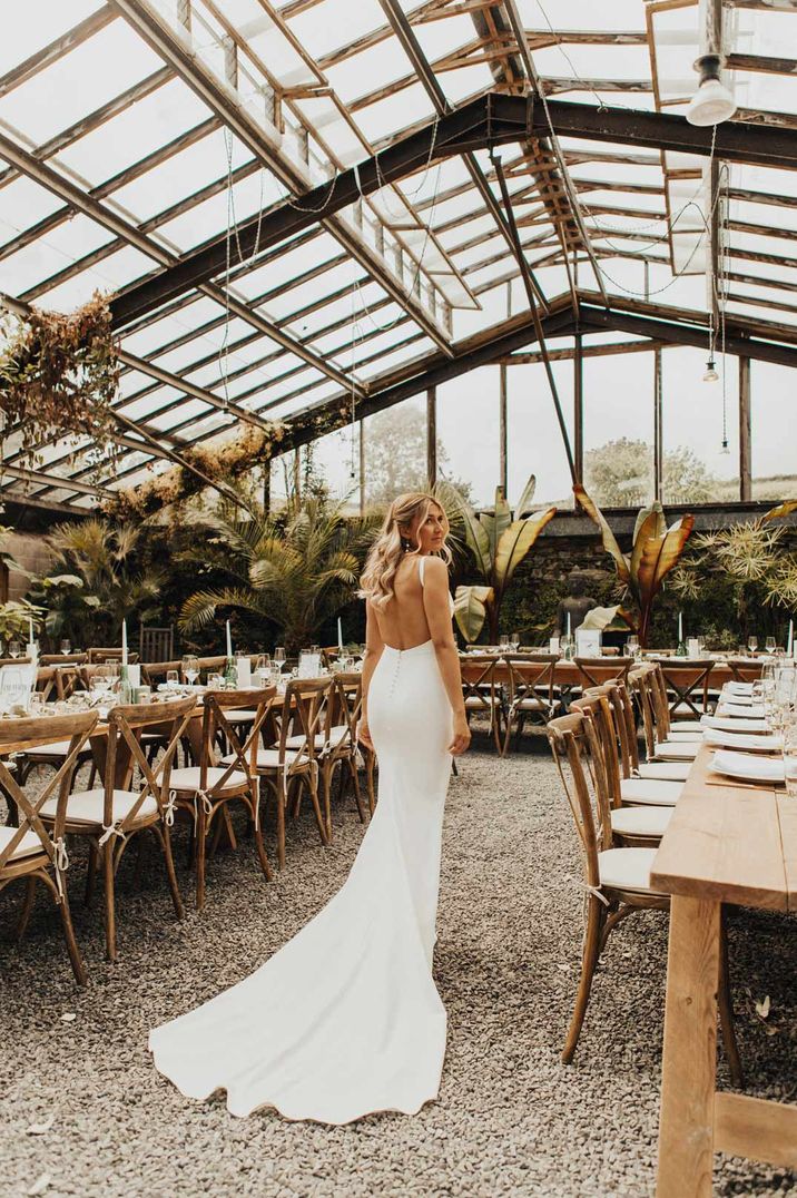 Bride in open back detail wedding dress walking through Anran glasshouse wedding venue with large tropical florals and neutral wedding tablescapes 