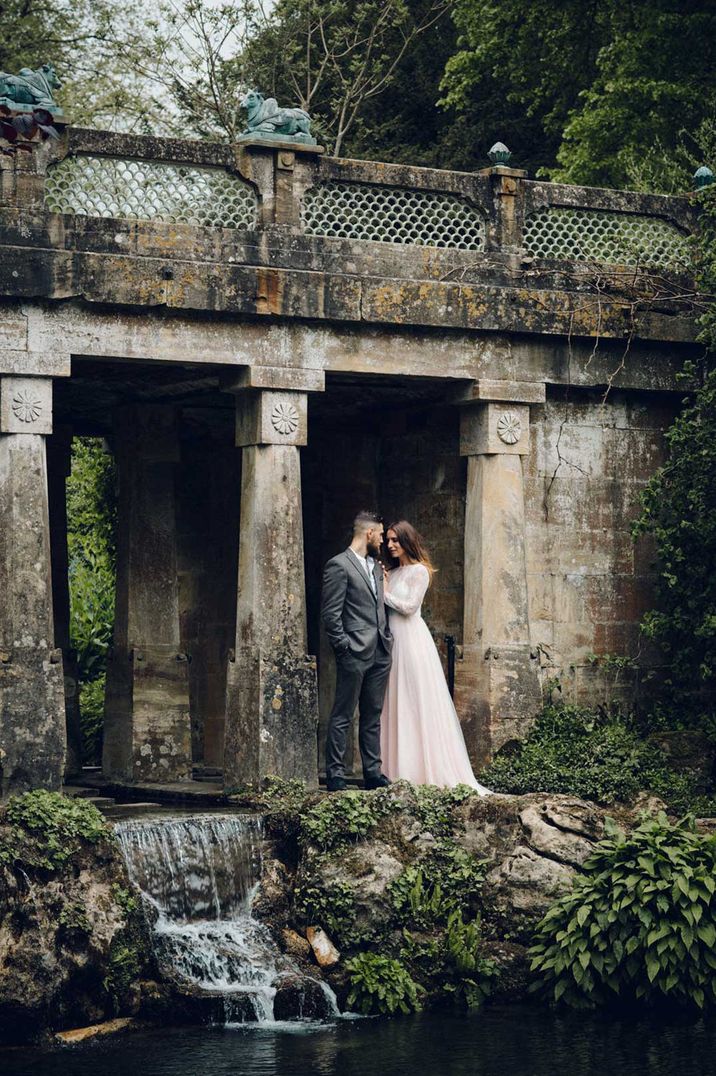 Bride in long sleeve wedding dress and groom in dark suit standing on the grounds of Sezincote glasshouse wedding venue Gloucestershire 