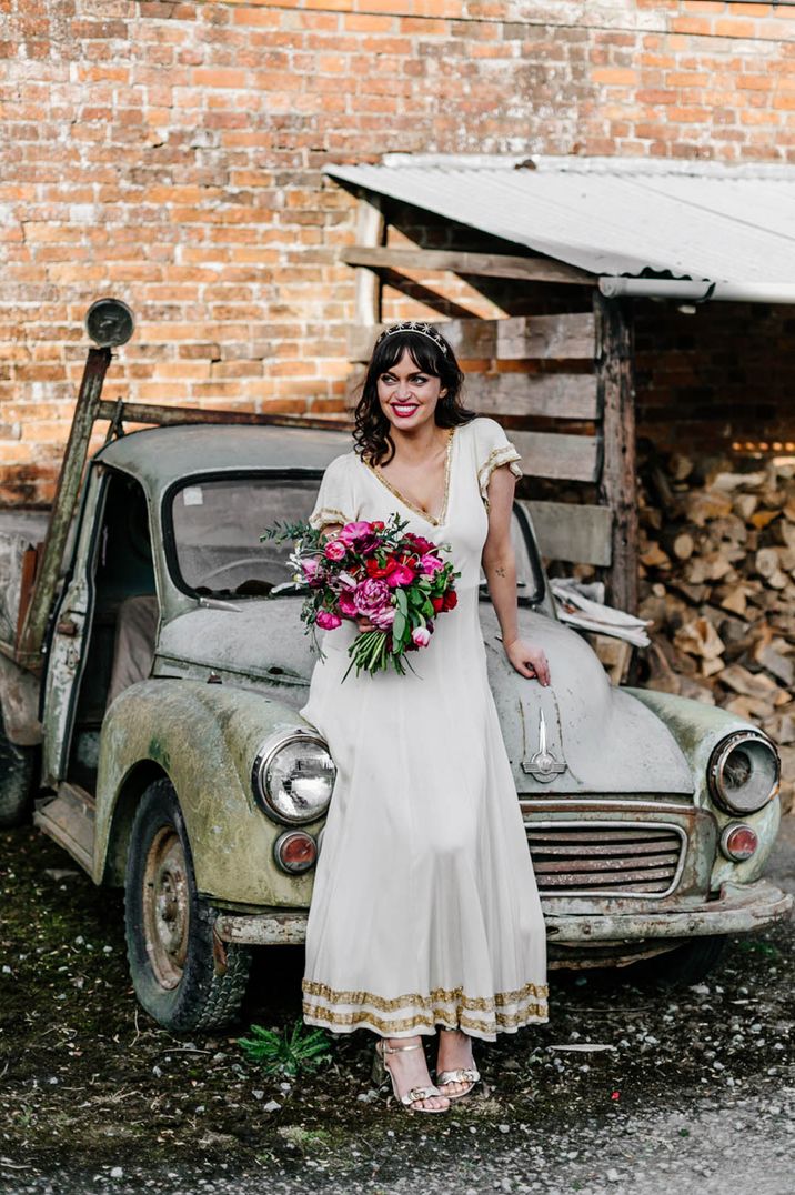 Bride in a vintage wedding dress with gold detailing and a pink and red wedding bouquet with a star tiara and bright red lipstick 