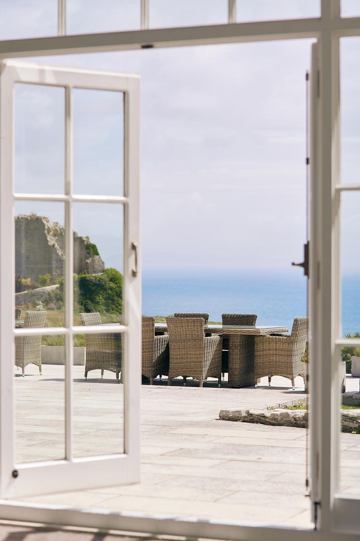 Window and door at Pennsylvania Castle Estate looking out onto a sea-front view with wicker outdoor chairs 