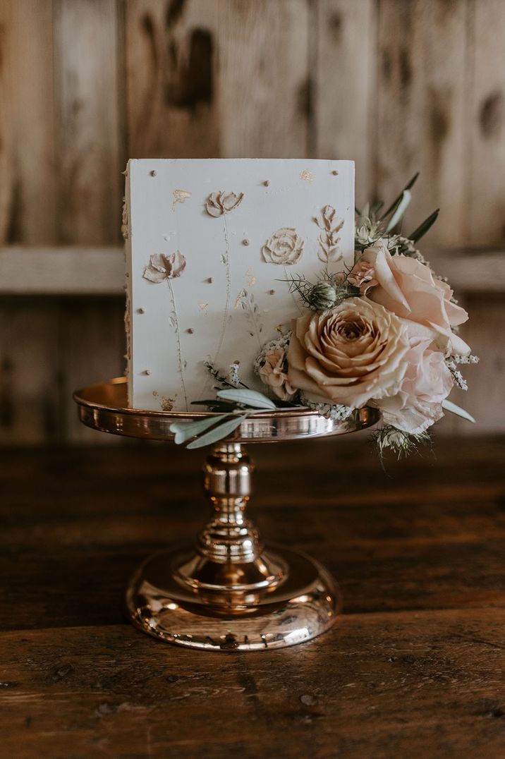 Square white iced wedding cake with neutral pink wedding flowers iced on the cake with neutral roses 