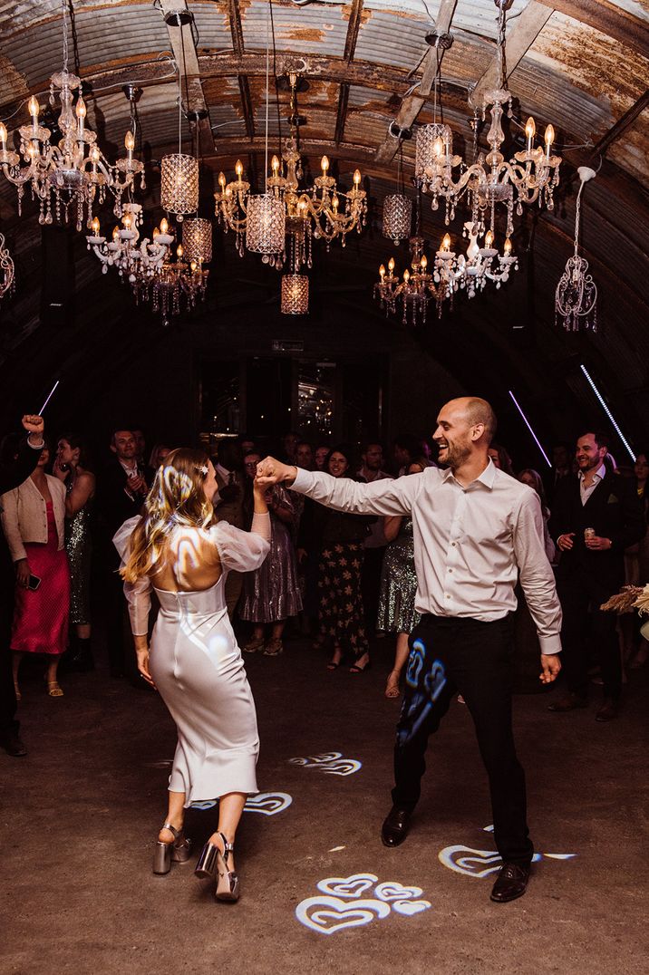 The happy couple dance underneath mismatched chandeliers for romantic moment 