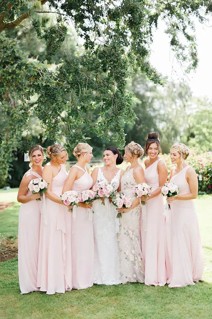 Bride posing with her bridesmaids wearing pale pink spring bridesmaid dresses 