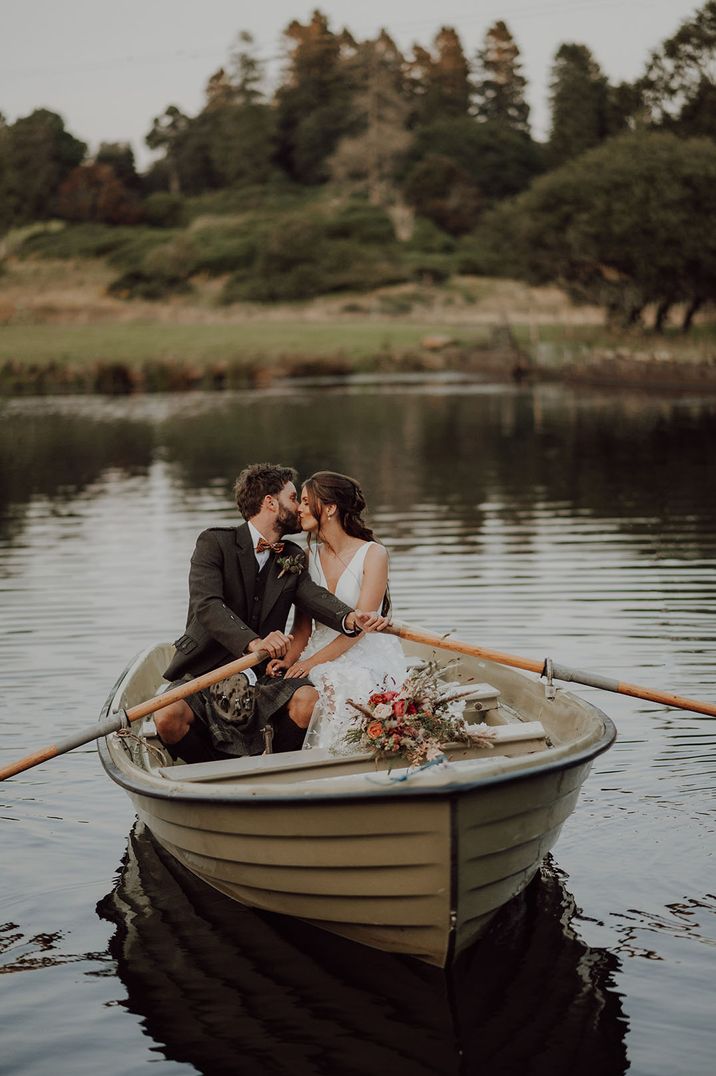 Couple in tan rowboat, bride in v neck wedding dress and groom in dark suit and burgundy bow tie