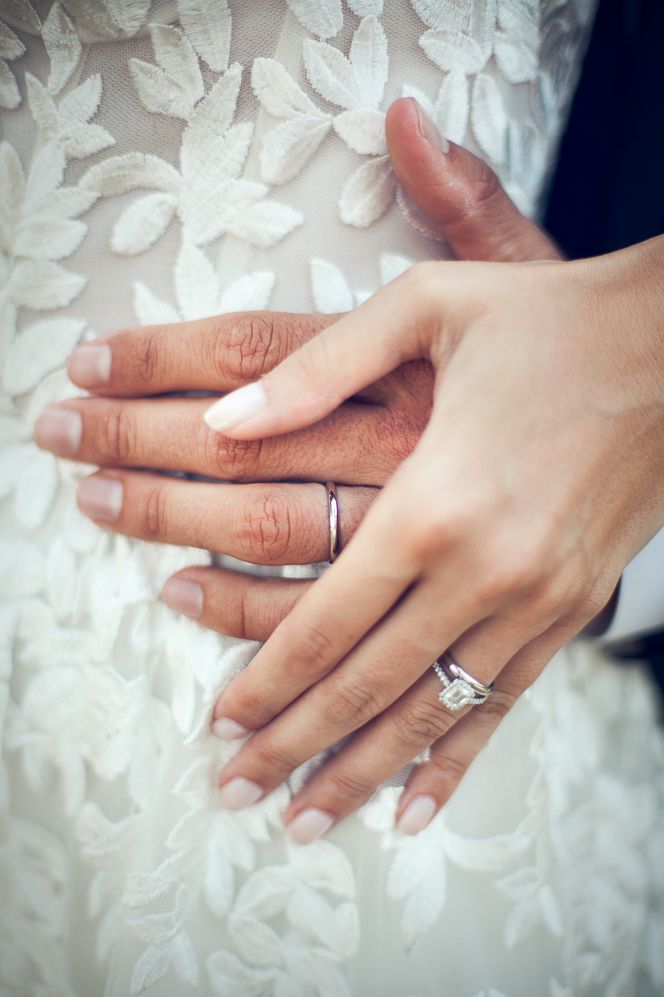 Bride in a lace Wedding dress holding hands with her groom showing off their platinum wedding bands and diamond engagement ring 