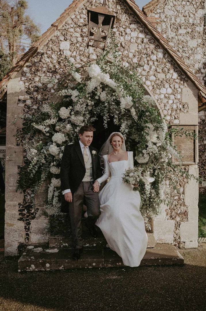 Bride in square neck wedding dress and groom by floral arch at Hedsor House